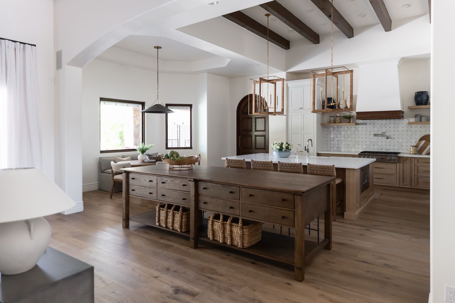 A warm oak kitchen with beamed ceiling, woven lanterns and a double island by Kimberley Kay Interiors
